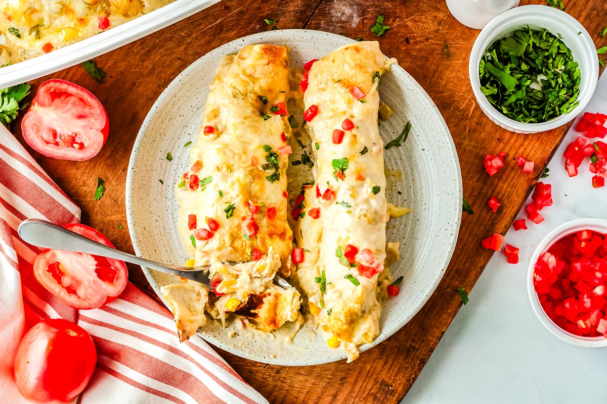 Two chicken enchiladas with green chiles and sour cream on a white plate and a fork digging into one of them.