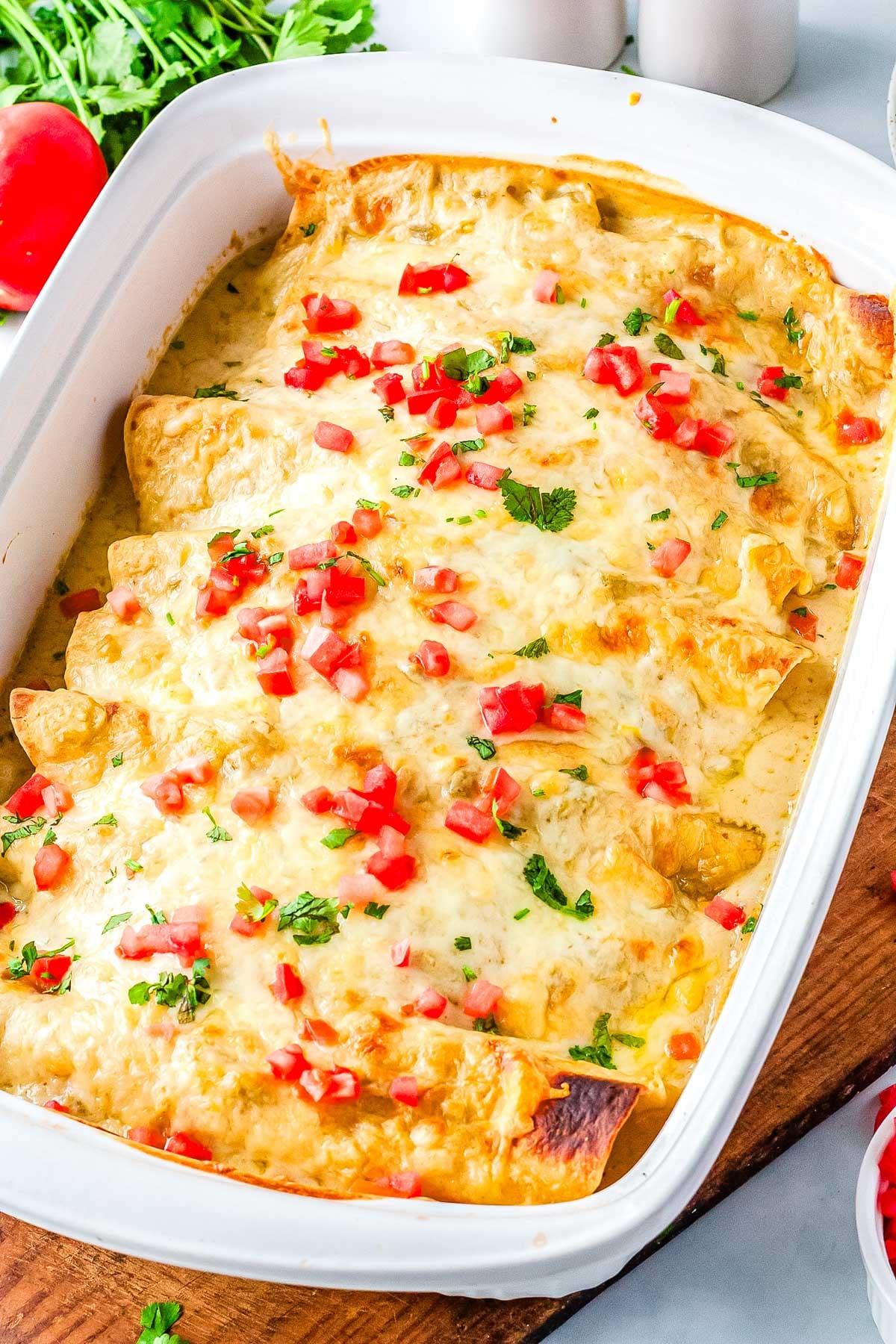 The finished Sour Cream Chicken Enchiladas Recipe in a casserole dish and garnished with chooped tomatoes and cilantro.