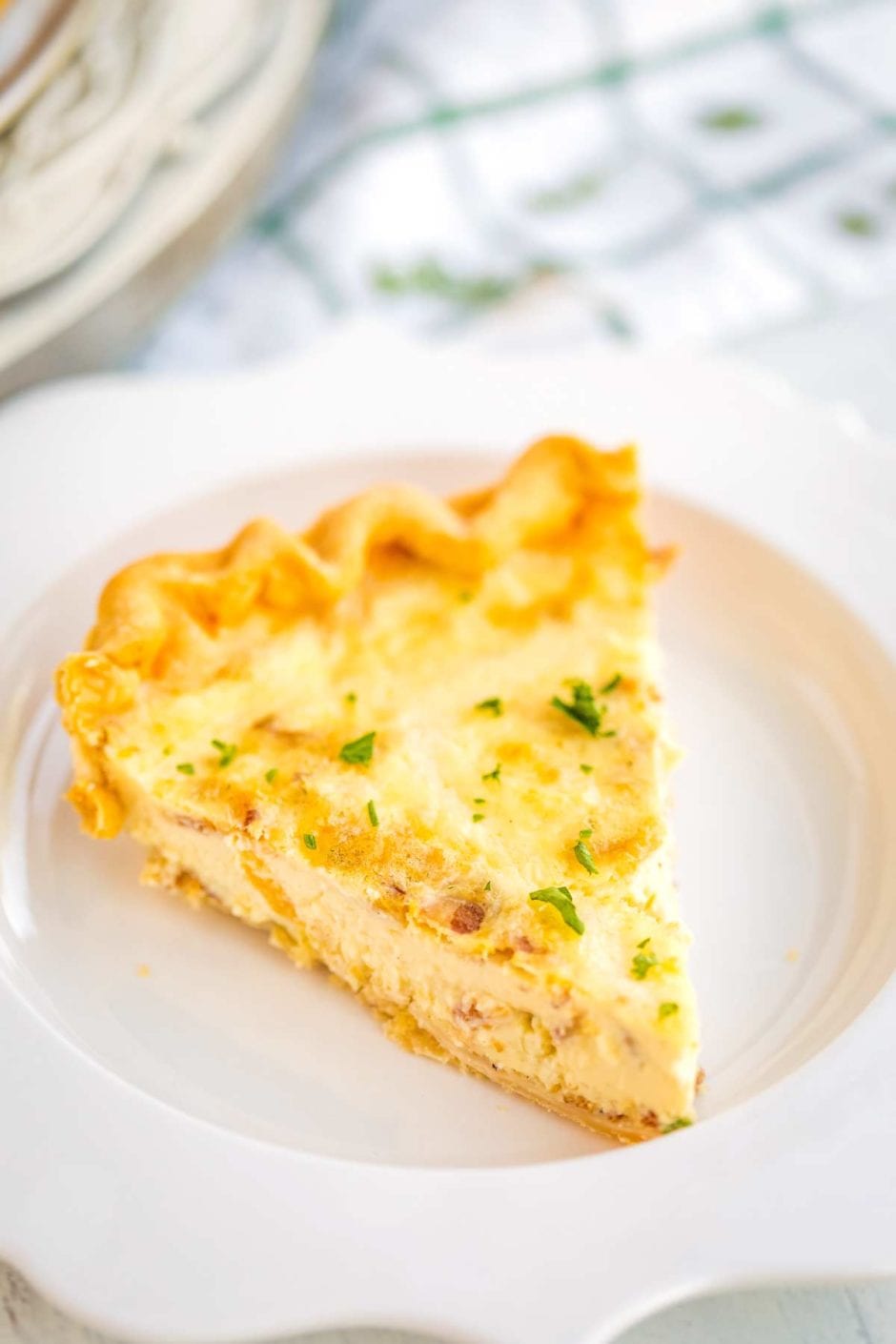 Close up picture of Homemade Quiche Lorraine slice on a white plate. 