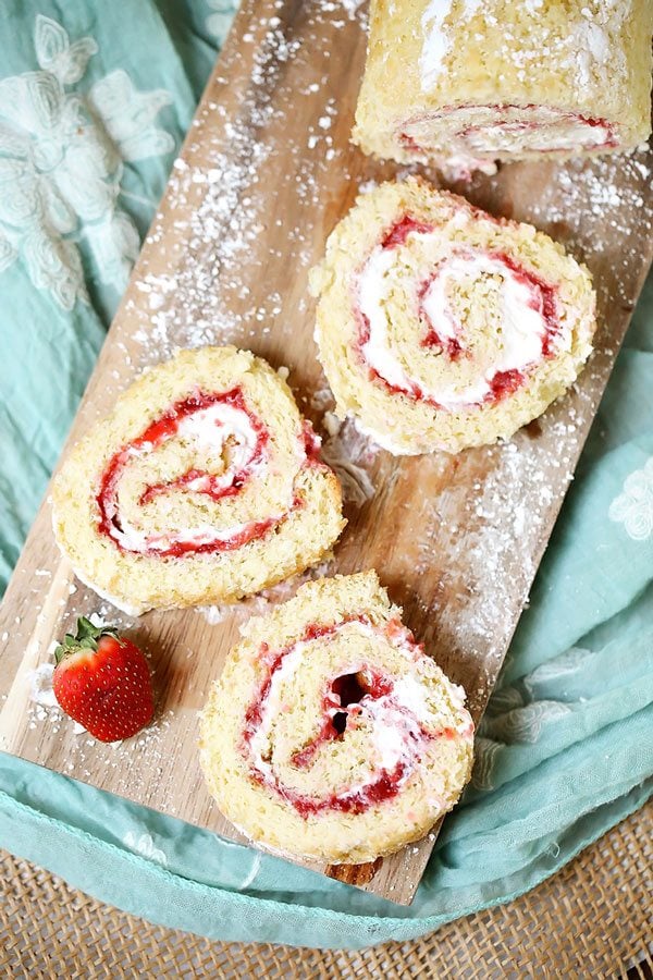 3 Slices of this strawberry shortcake roll on a wooden cutting board.