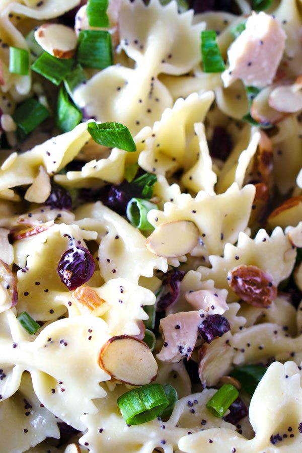 Close up picture of bowl tie pasta with almonds, poppy seed dressing, dried cranberries, chicken, and green onions. 