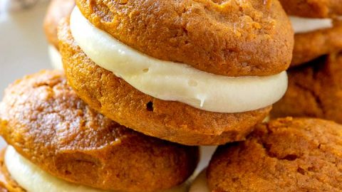A plate of pumpkin whoopie pies stacked on top of each other.