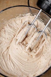 process shot of beating cinnamon cream cheese frosting with a handheld mixer