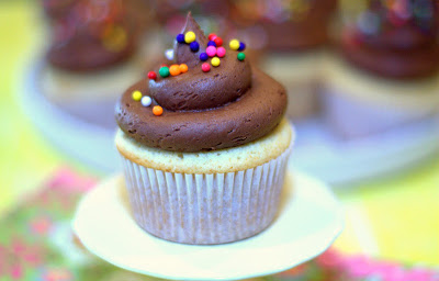 a close up of a yellow cupcake with chocolate buttercream frosting on a cake stand