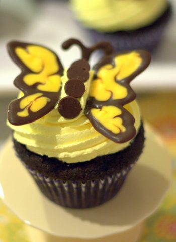 A close up of a dark chocolate butterfly cupcake on a cake stand