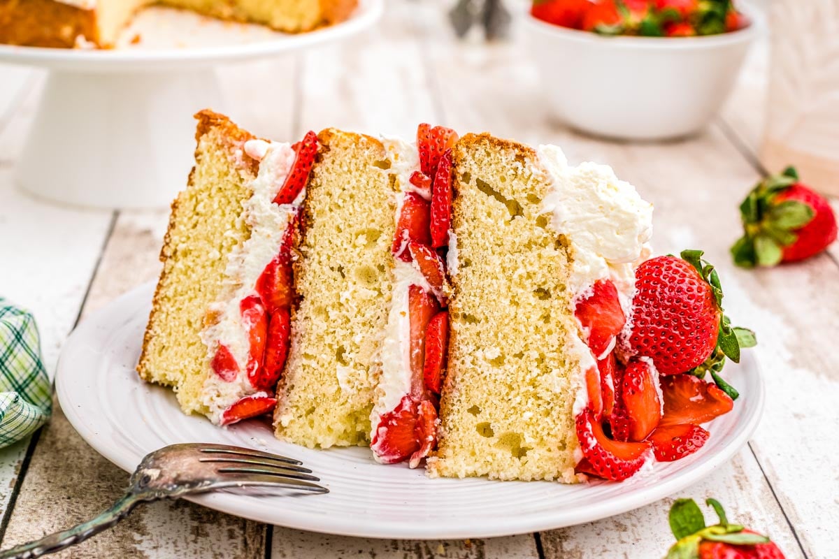 A piece of strawberries and cream cake on a white plate.