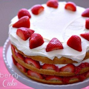 A layered strawberry cream cake on a cake stand with text overlay for Pinterest