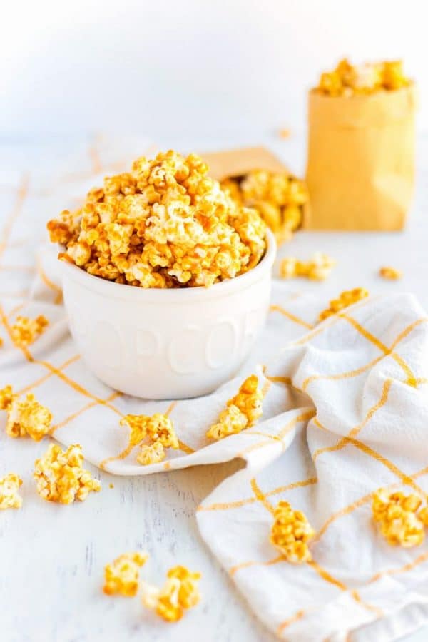 Caramel Corn in a white bowl and some pieces scattered on a tabletop. 