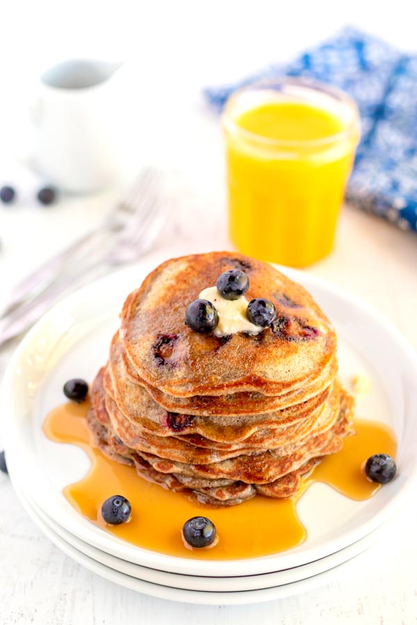 A stack of pancakes with butter, a drizzle of syrup, and fresh blueberries.