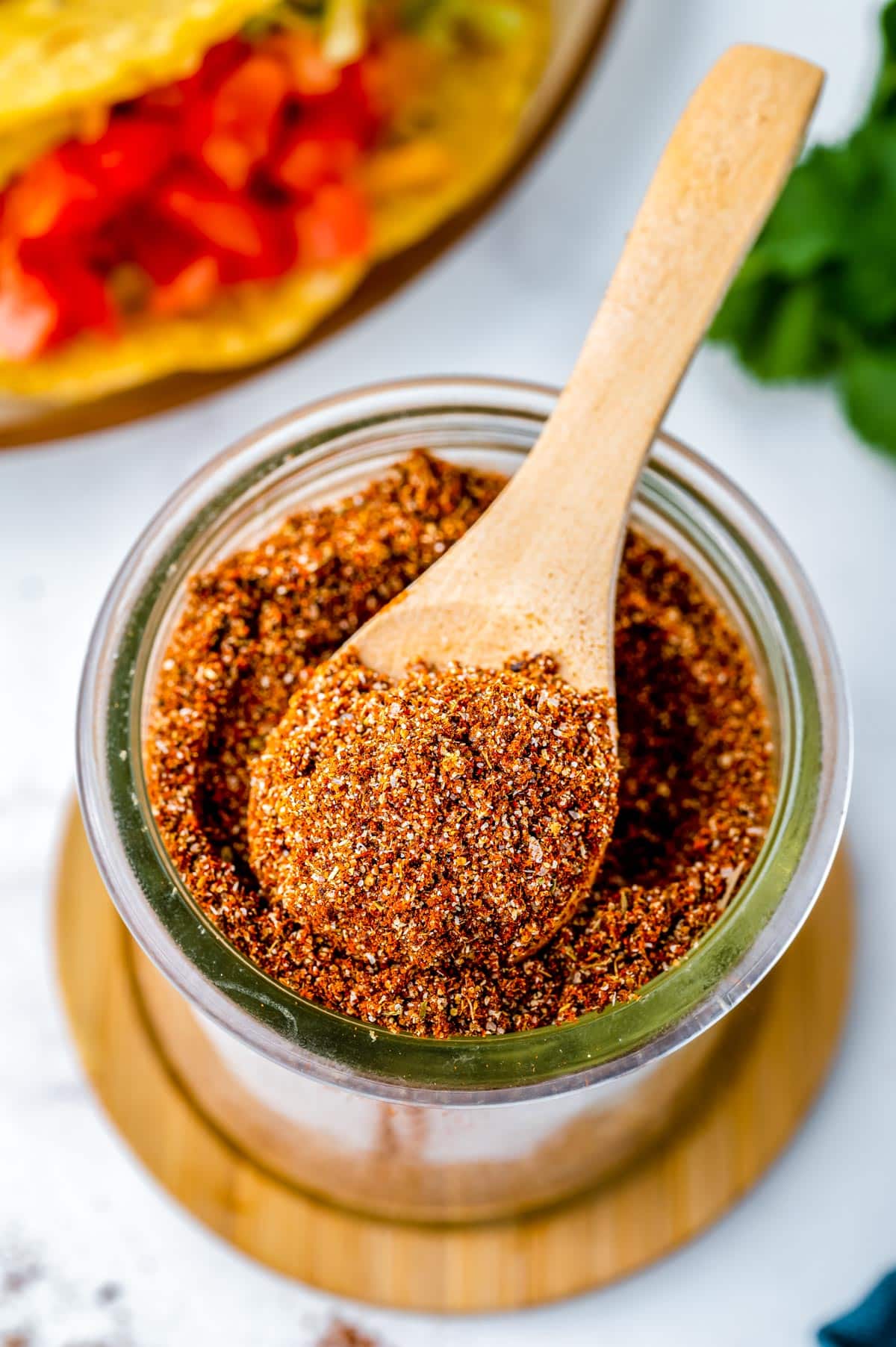 A wooden spoon scooping some taco seasoning from a glass jar. 