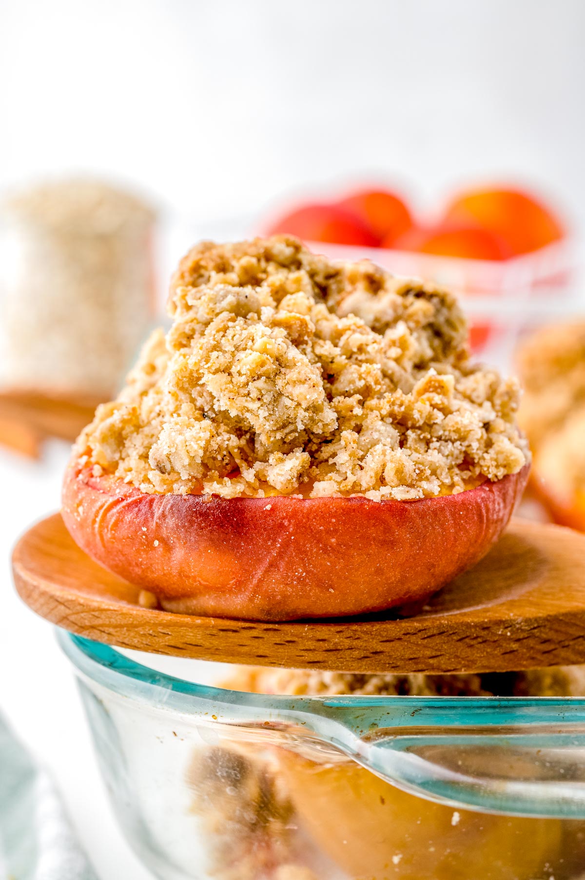 A wooden serving spoon picking up one of the Baked Peaches with Oatmeal from the baking dish.