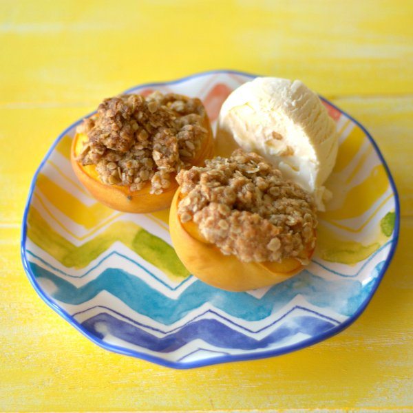 Baked Peaches with Oat crumble topping and a scoop of vanilla ice cream on a plate