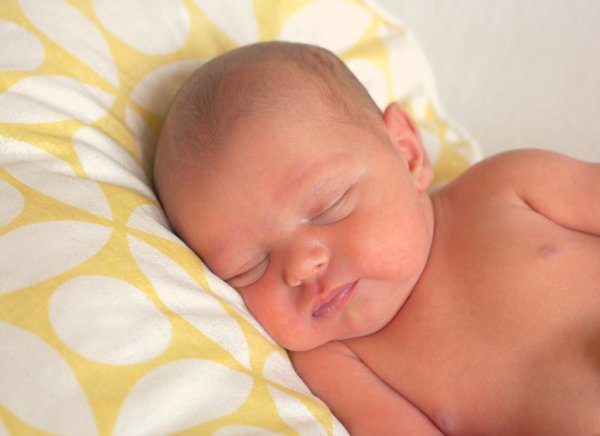 A baby sleeping on a yellow and white pillow. 