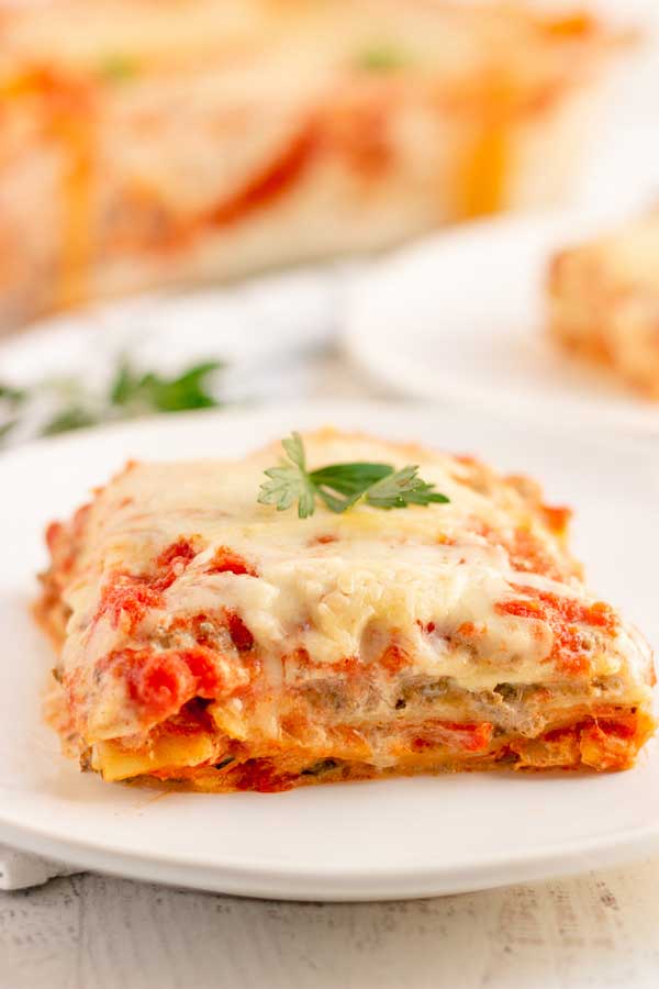 A slice of Lasagna with Italian Sausage on a white plate. 