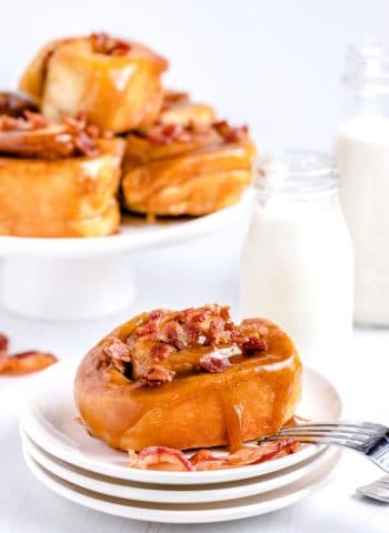A glistening bacon sticky bun with caramel glaze on a white plate.