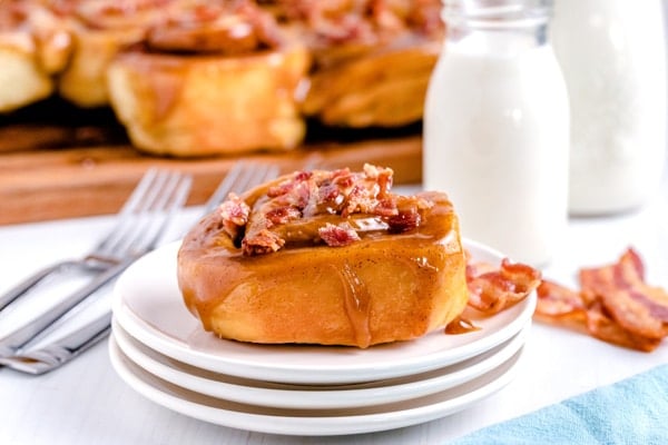 A sticky bun with bacon on a white plate with milk in the background. 