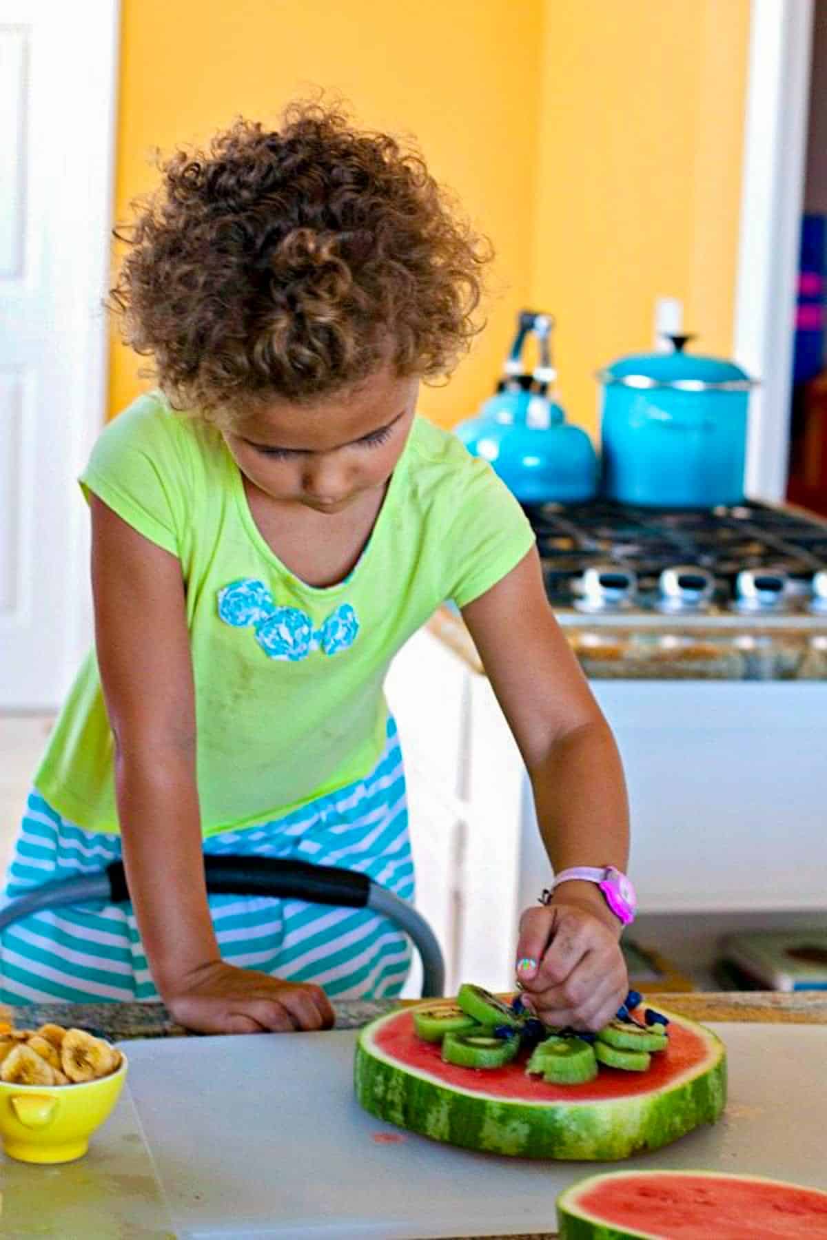 A 4-year-old girl adding toppings to a Watermelon Pizza.