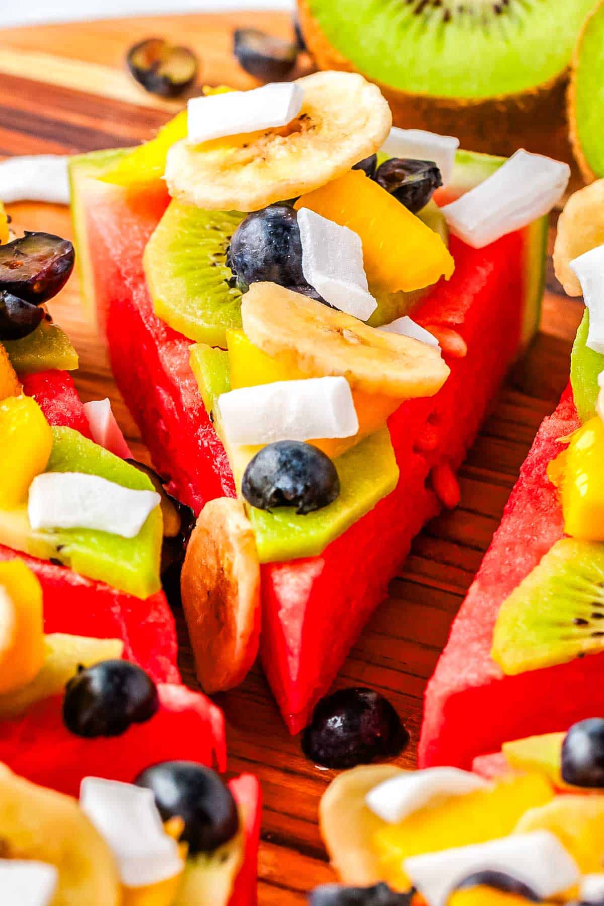A close up picture of a slice of Watermelon Pizza on a wooden cutting board. 
