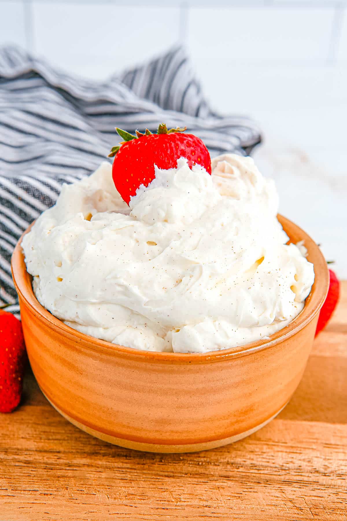 A bowl of the Cream Cheese Frosting with Whipped Cream in a bowl and a strawberry in it.