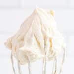 The finished Cream Cheese Frosting With Whipped Cream on a whisk and being held upside down.
