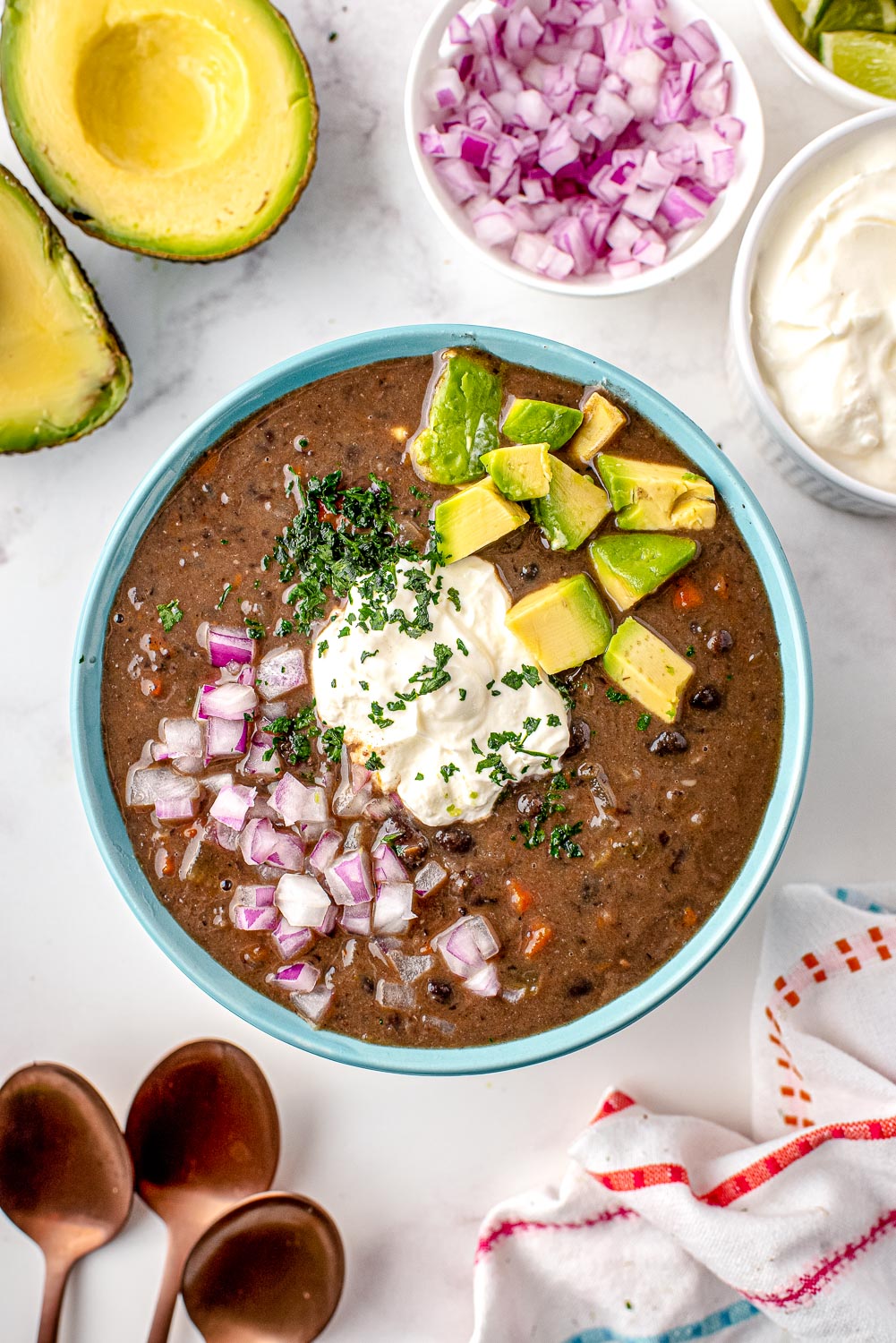 Black Bean Soup made from scratch in a blue serving bowl topped with diced avocado, red onion, and sour cream.