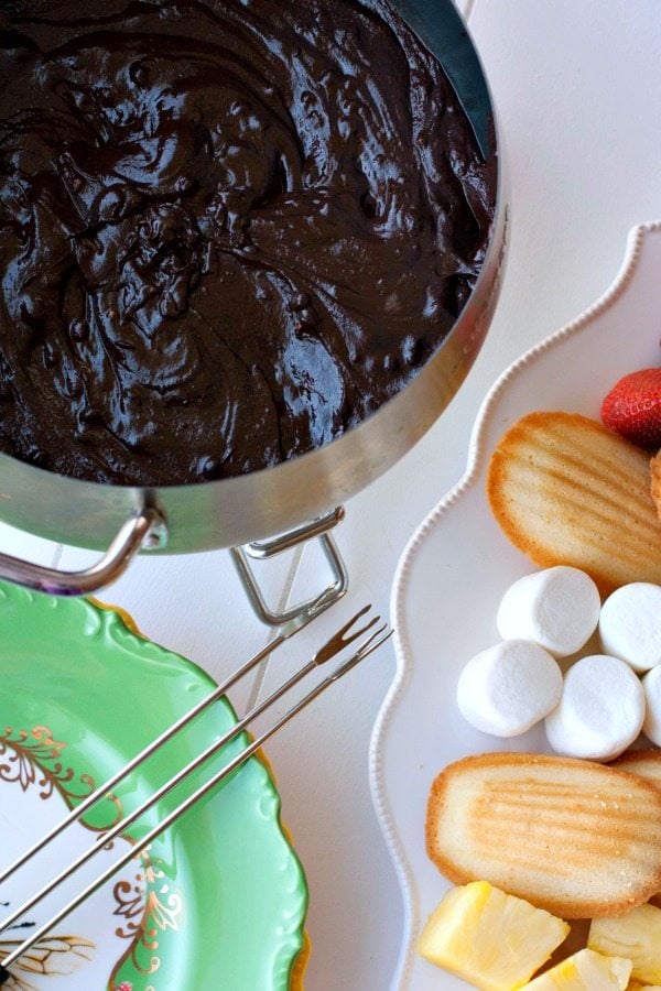 Chocolate fondue in a fondue pot with items to dip on a plate next to it