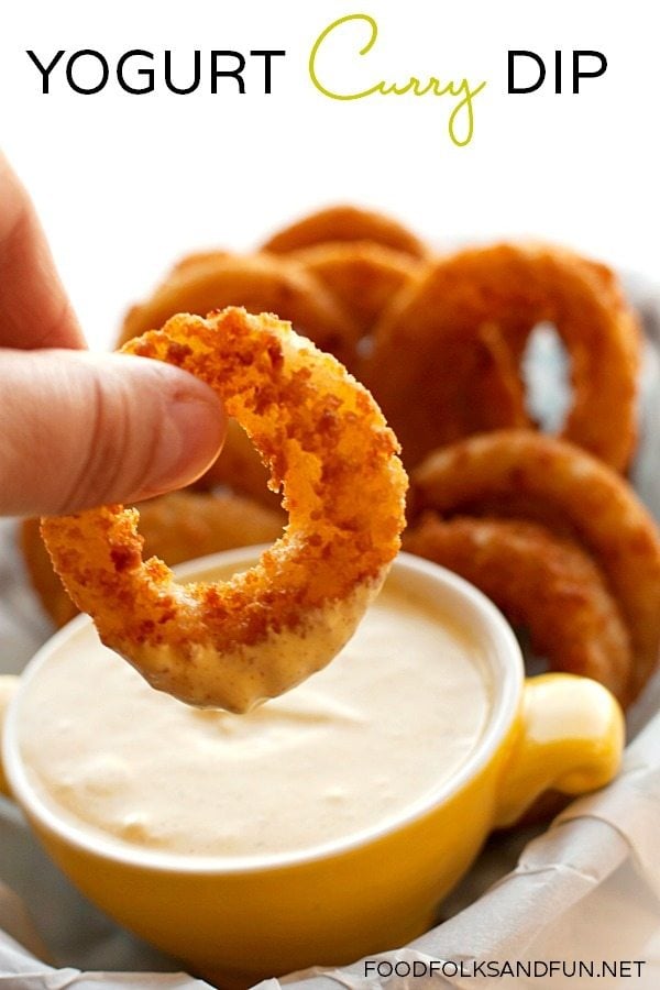 An onion ring being dipped into curry dip. 