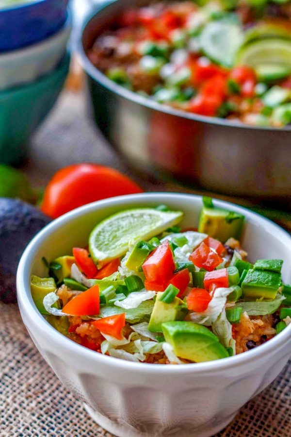 Chicken burrito bowl garnished with lime wedge, green onion, tomato, and avocado.