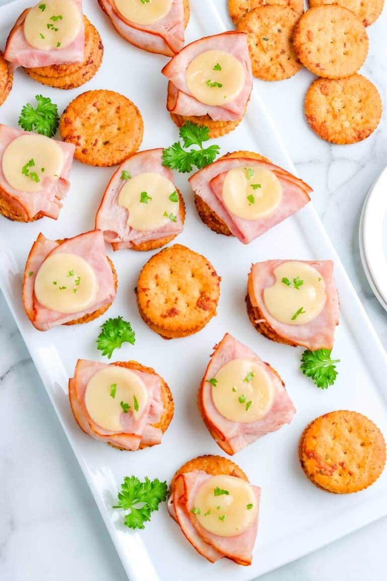 Ranch crackers on a white platter, some with ham and cheese on them.
