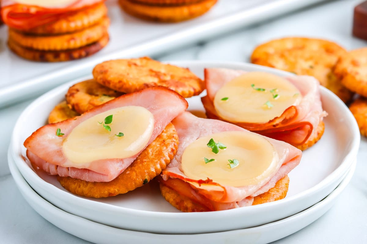 Ranch Crackers with ham and cheese on them on a white plate.