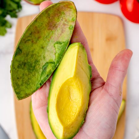 A cut and peeled avocado in a hand.