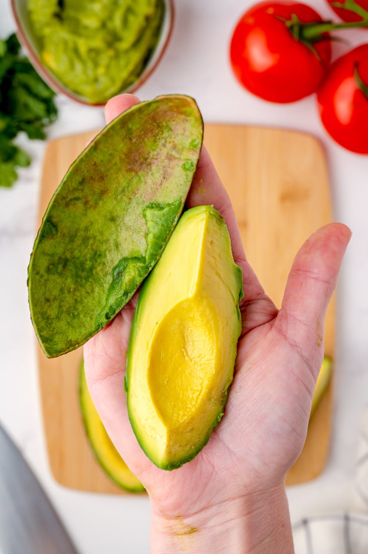 A cut and peeled avocado in a hand.
