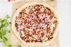 Top the pizza with cheese, chicken, bacon, and red onion and bake until golden.