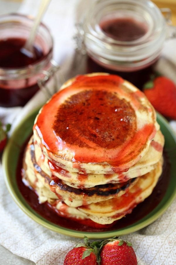A large stack of pancakes with strawberry pancake syrup on them.