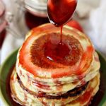 A spoonful of strawberry syrup pouring over a stack of pancakes