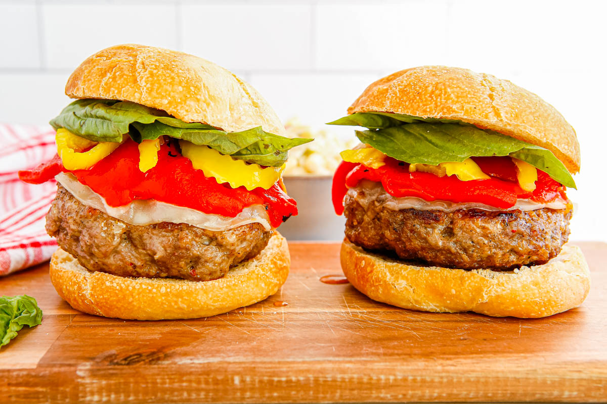 Two of the finished Italian Sausage Burgers on a wooden cutting board.