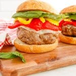 A finished Italian Sausage Burger on a wooden cutting board with roasted peppers and basil on the burger.