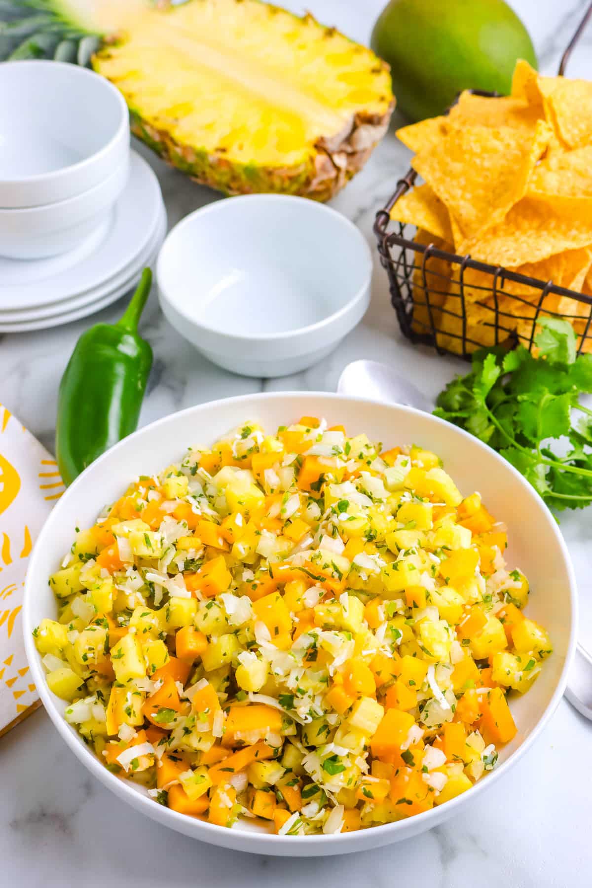 Pineapple Mango Salsa in a white serving bowl with tortilla chips in the background. 