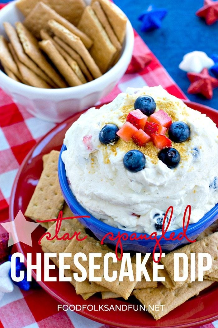 Cheesecake Dip with cut up berries in a blue bowl surrounded by graham cracker pieces. 