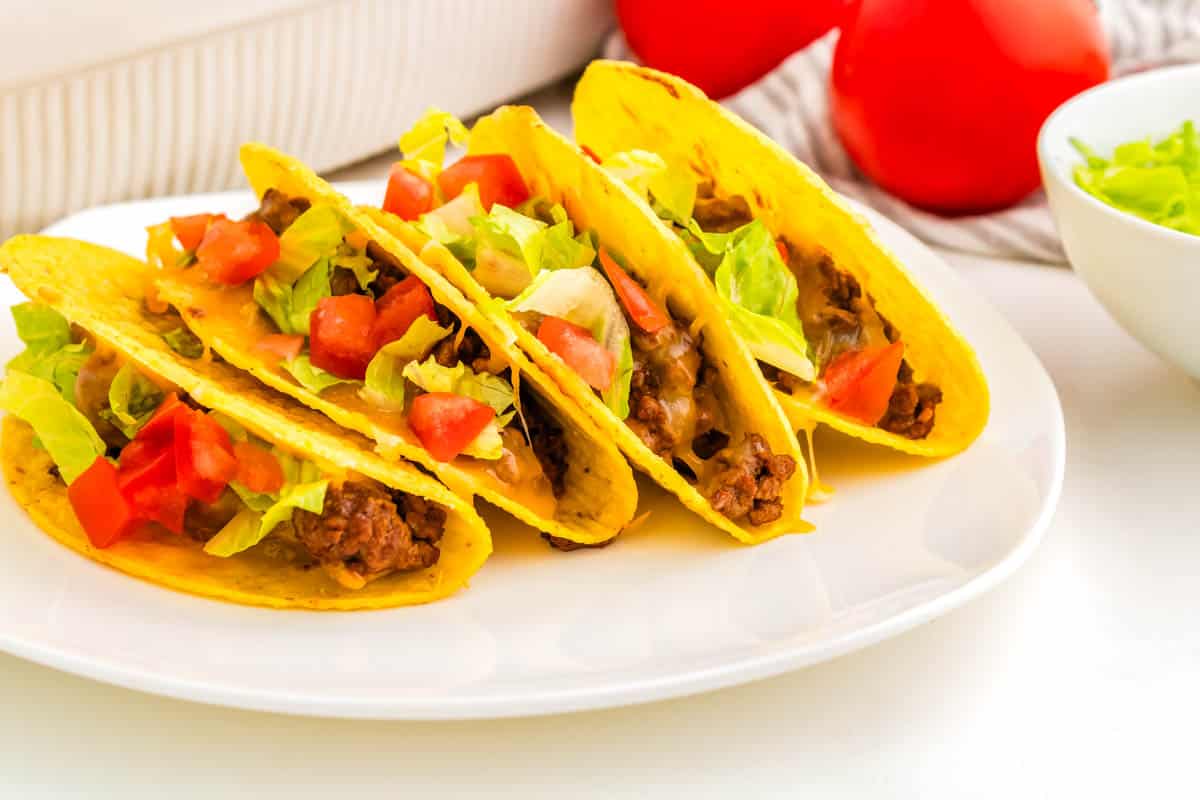 Four hard shell tacos on a white plate.