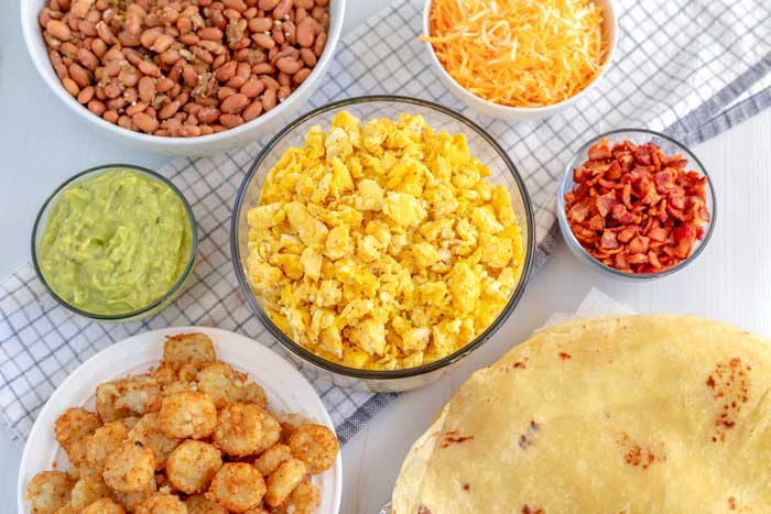 All of the ingredients in bowls needed to make breakfast burritos.