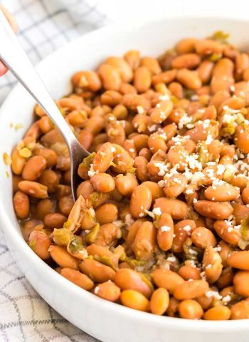 Pinto beans with green chile in a large bowl with serving spoon.