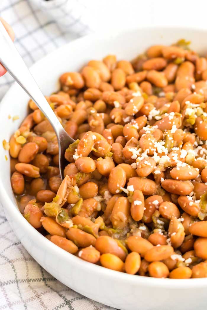 Pinto beans with green chile in a large bowl with serving spoon.