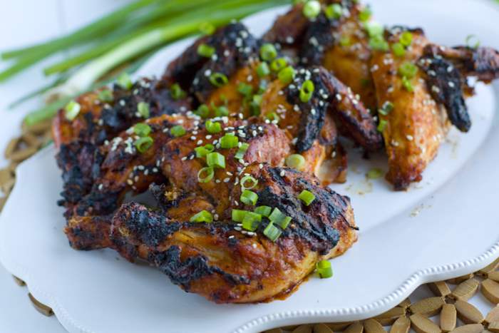 Game hens on a white platter sprinkled with chopped green onions and sesame seeds. 