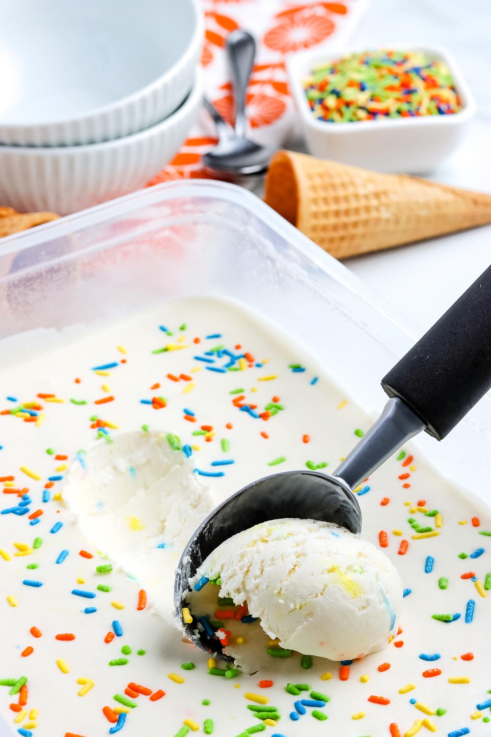 Funfetti Birthday Cake Ice Cream in a container being scooped with an ice cream scoop.
