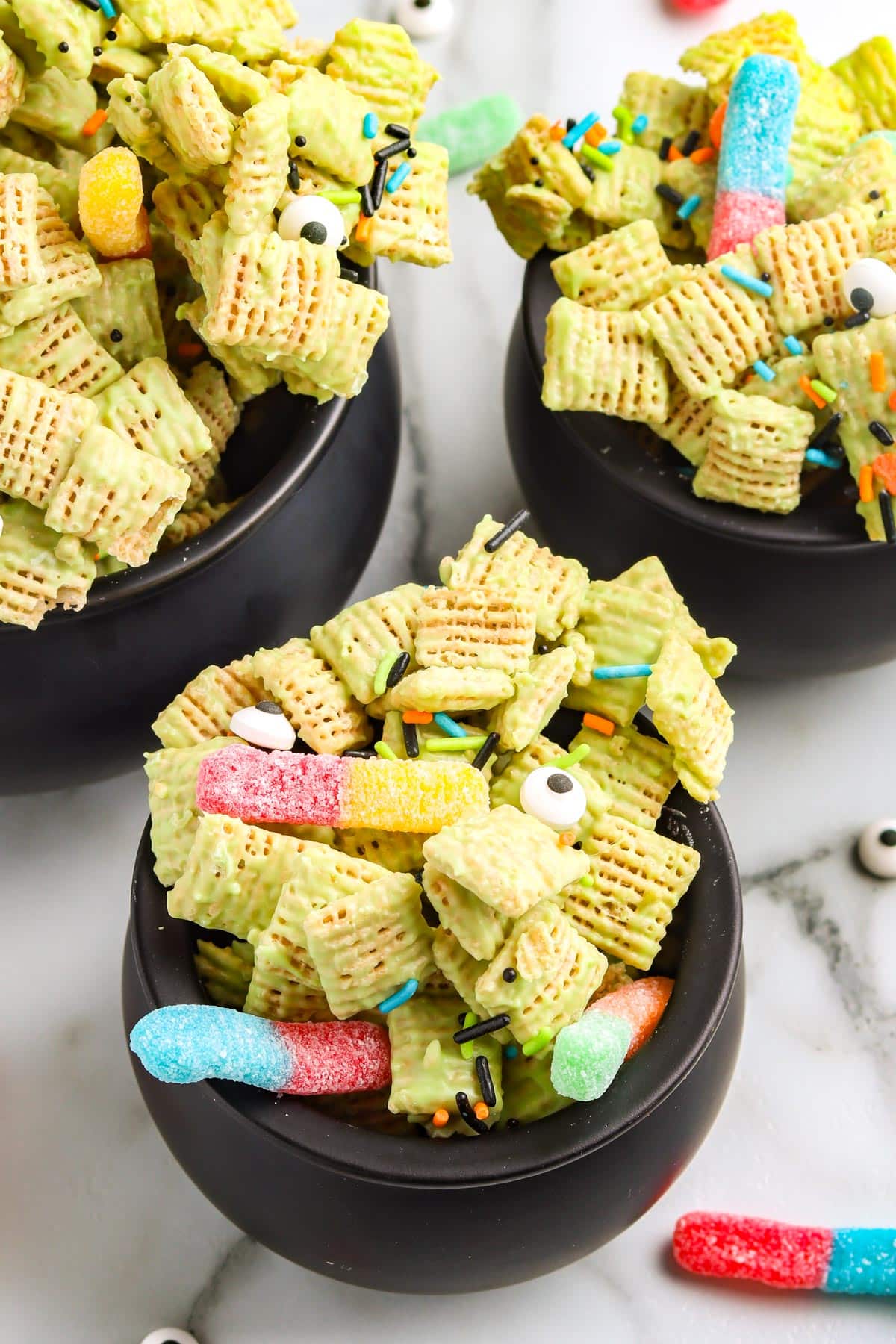 Finished chex mix in small, black, plastic cauldrons for Halloween.
