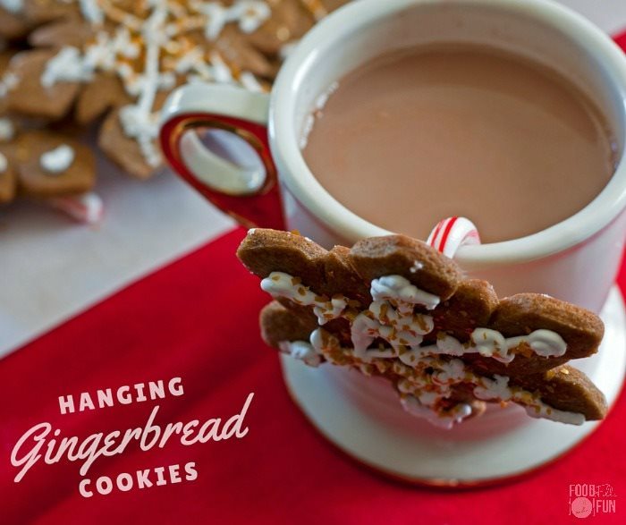 Gingerbread cookie with a small candy cane attached, and hanging from a cup of cocoa. 