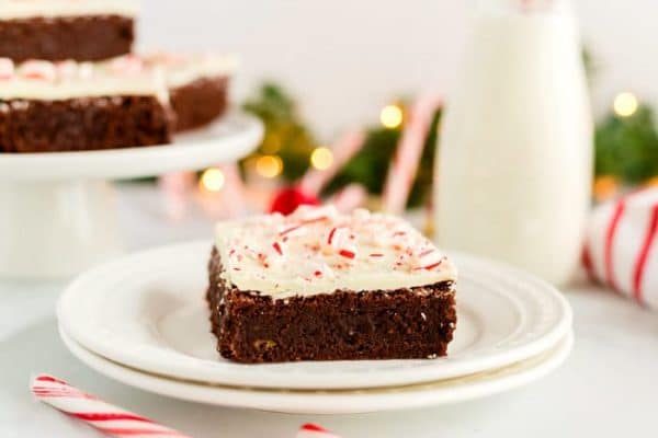 A brownie on a white plate with milk and candy canes in the background. 