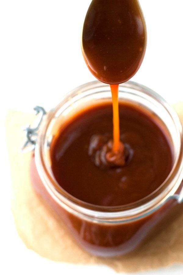 Caramel drizzling off of a spoon into a jar of sauce. 