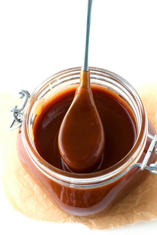 A spoonful of caramel sauce from a jar full of caramel